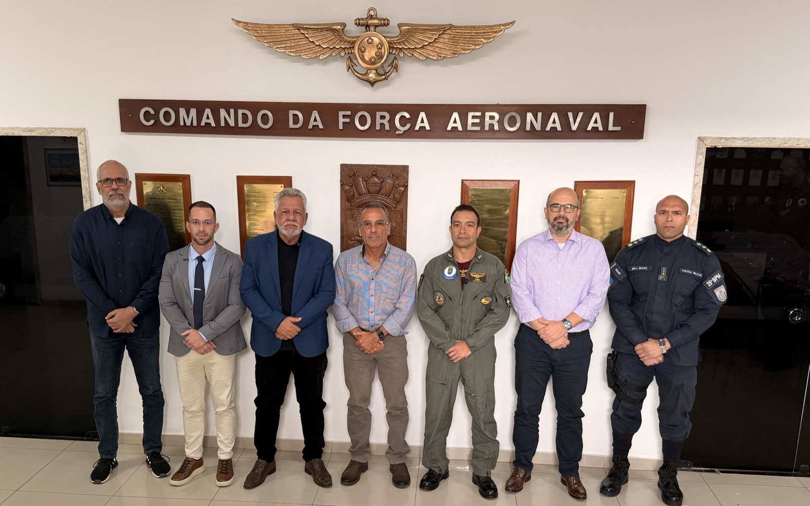 Comitiva do CONDERLAGOS e oficiais diante da placa do Comando da Força Aeronaval.